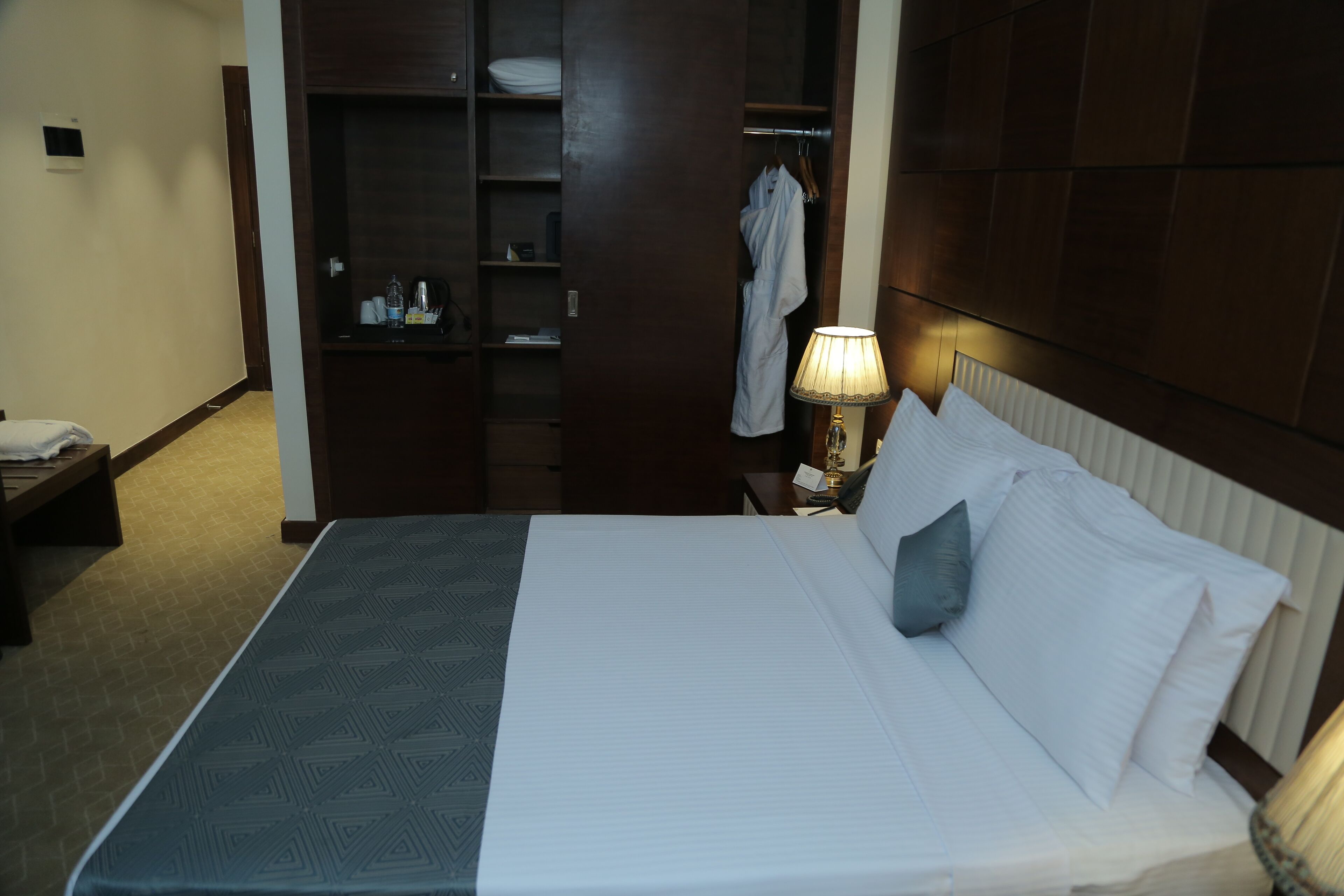 Una habitación de hotel con cama, mesita de noche, lámpara y armario.