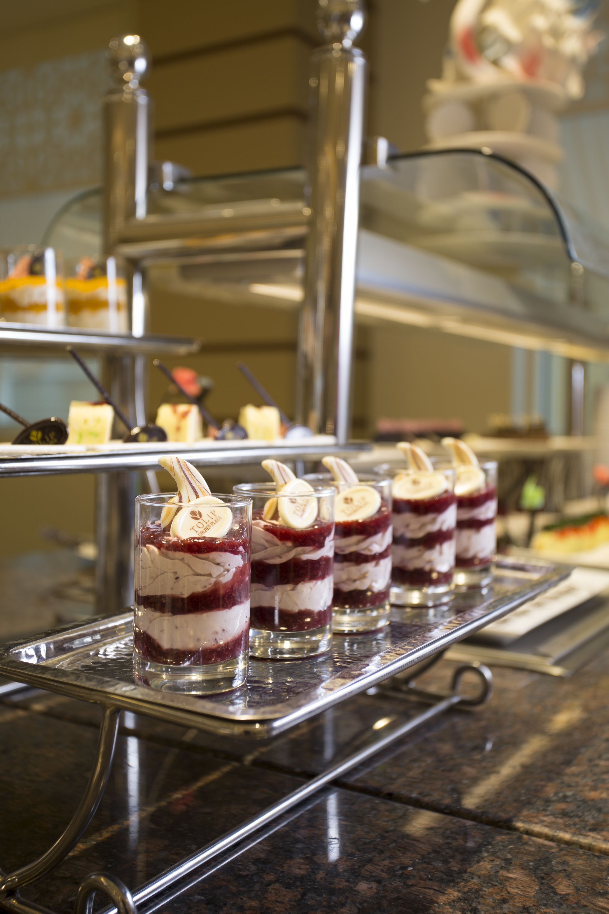 Vasos de postre con pastel en capas y rodajas de plátano sobre una bandeja metálica.