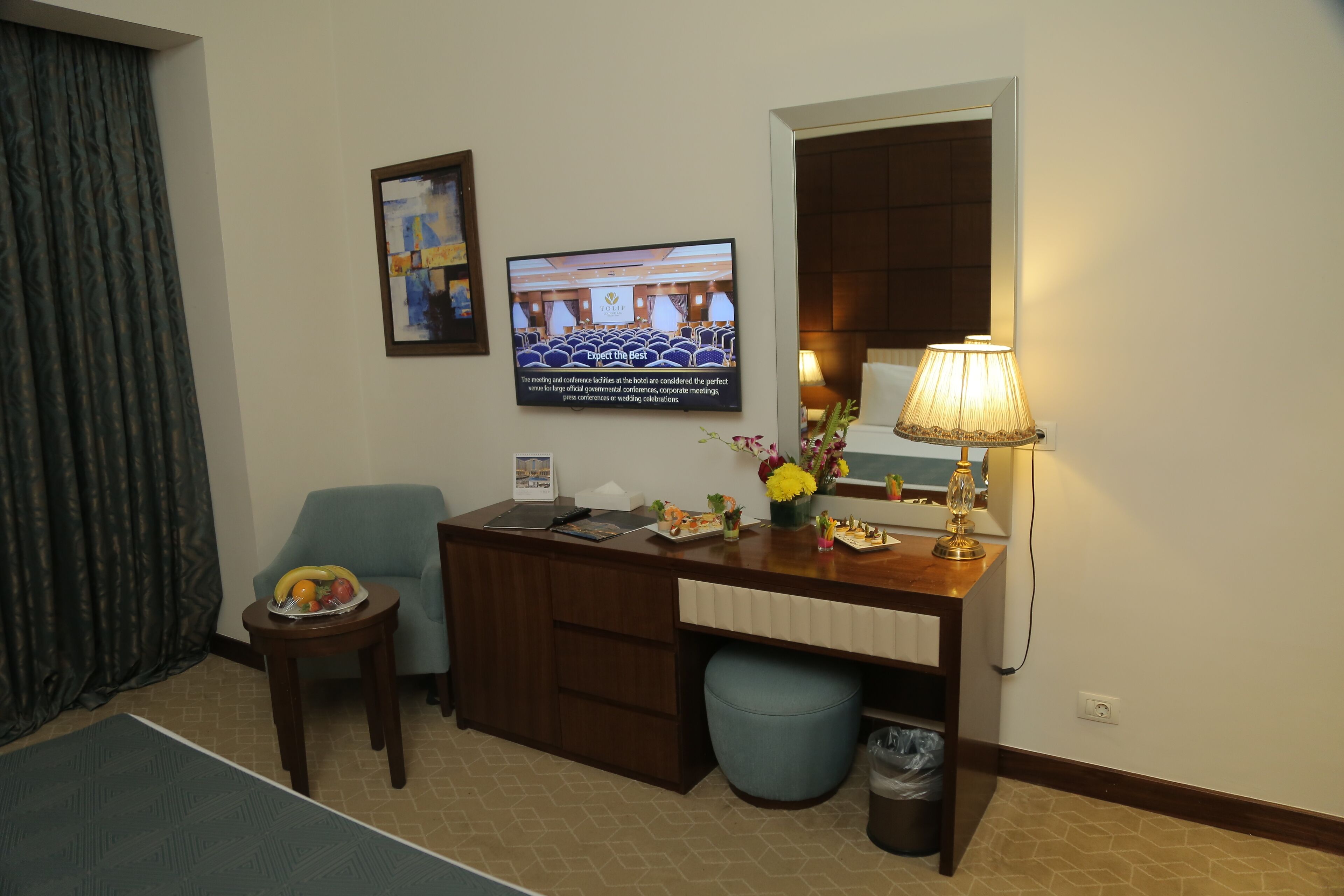 Een hotelkamer met een bureau, een stoel, een televisie, een lamp en een prullenbak.