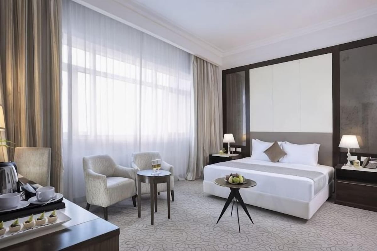 Habitación de hotel con una cama grande, dos sillones, una mesita y un escritorio con una lámpara.