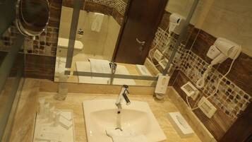 A bathroom with a large mirror, a sink, and two hair dryers on the wall.