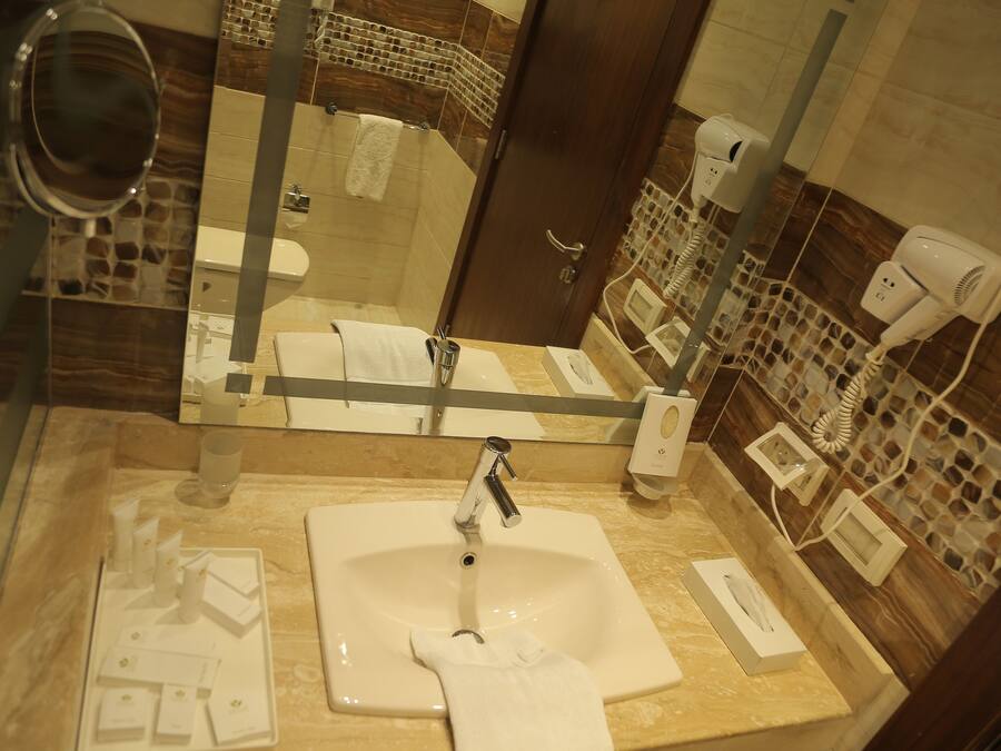 A bathroom with a large mirror, a sink, and two hair dryers on the wall.