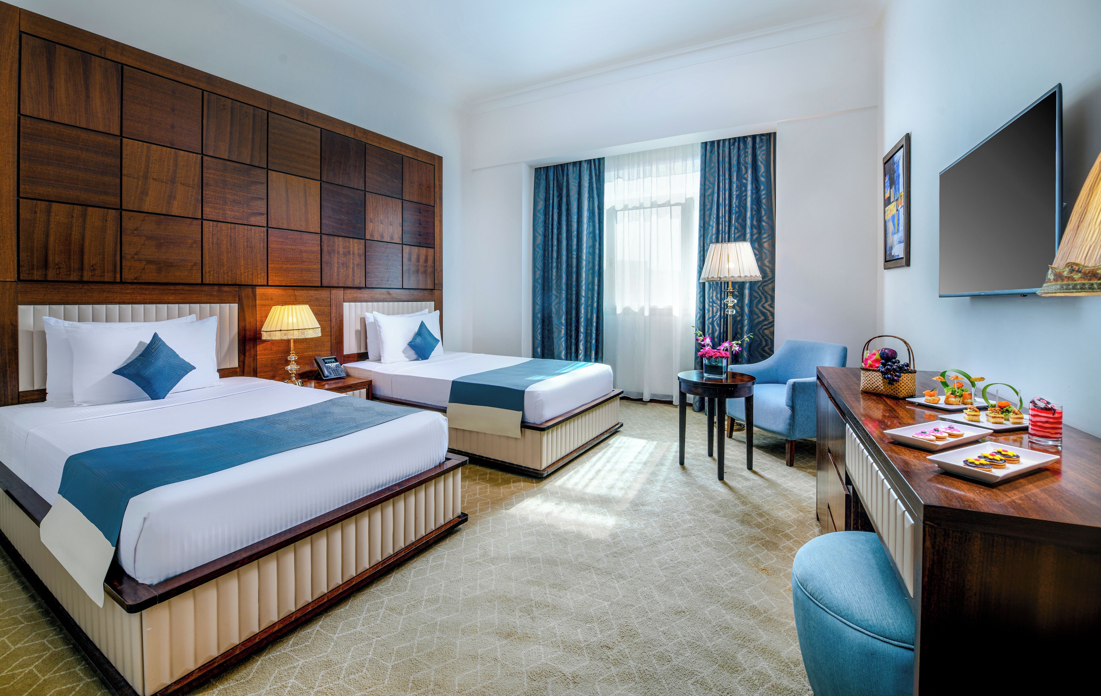 Een hotelkamer met twee bedden, een bureau, een stoel, een televisie en een raam met gordijnen.