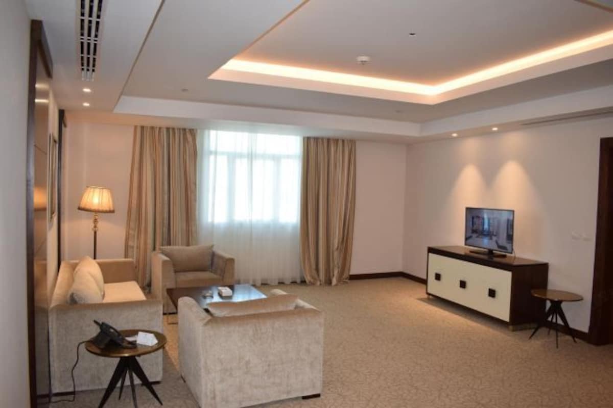 A hotel room with a sofa, armchair, coffee table, TV, and a lamp.