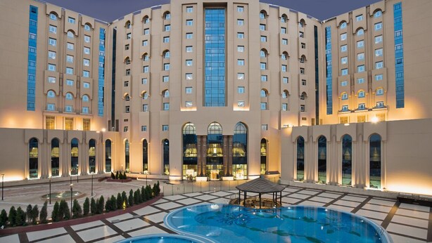 Un hotel con una gran piscina central, varios pisos y una entrada destacada.