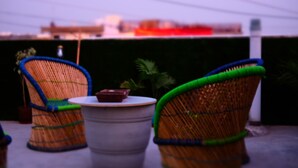 A wicker chair with a cushion, a small table, and a potted plant. - Amigos India - Hostel (New Delhi)