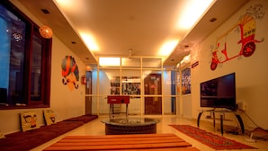 A modern living room with a glass coffee table, wooden benches, and a flat-screen TV. - Amigos India - Hostel (New Delhi)