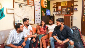 A group of people sitting on a couch in a room with a bulletin board, a tire wheel decoration, and various signs. - Amigos India - Hostel (New Delhi)