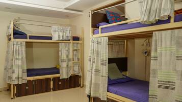 Ein Schlafsaalzimmer mit Etagenbetten, Vorhängen und einem kleinen Schreibtisch mit Lampe.