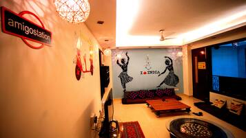A modern living room with a sign reading "amigostation," a wall mural of dancers, a sofa, a coffee table, and a small fire pit.