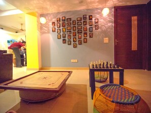 A room with a shuffleboard table, a foosball table, and a wall decorated with framed pictures. - Amigos India - Hostel (New Delhi)