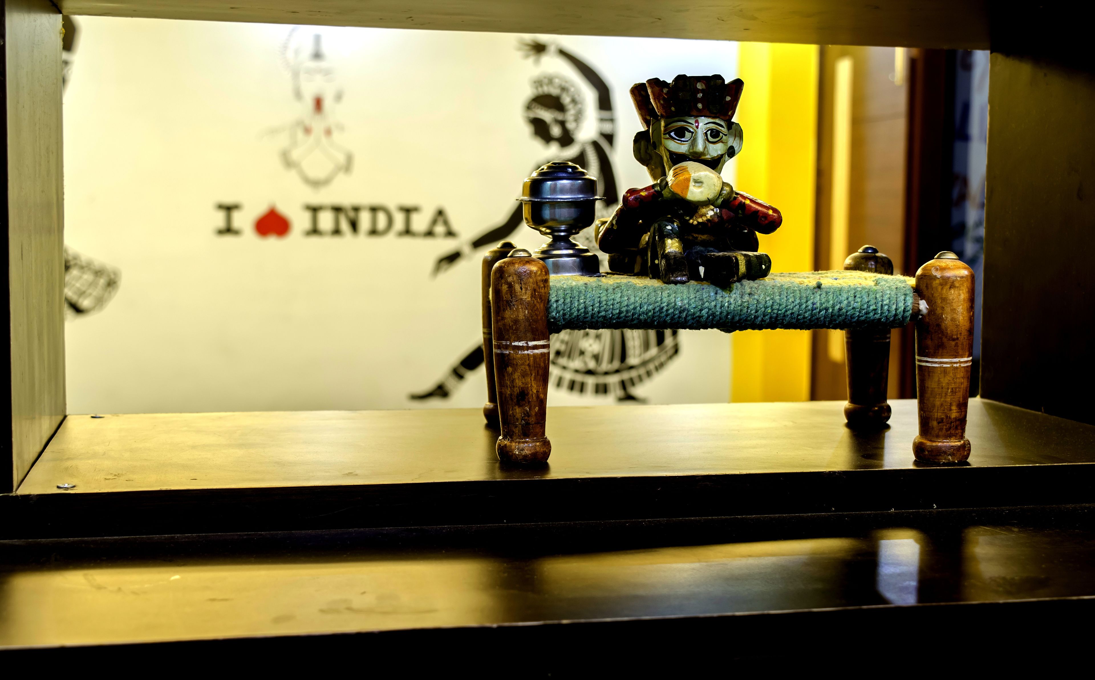 A small wooden table with a blue cloth and two wooden stools. In the background, there is a wall with a logo and the text "I ❤️ INDIA".