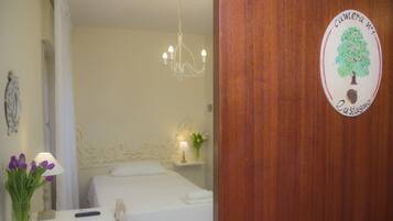 Habitación de hotel con una cama, una mesita de noche con lámpara, un jarrón con flores y una puerta de madera con un cartel.