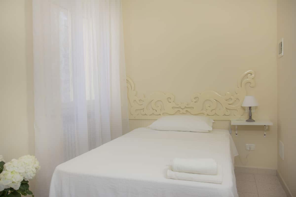 A neatly made bed with a white headboard and a bedside table with a lamp.