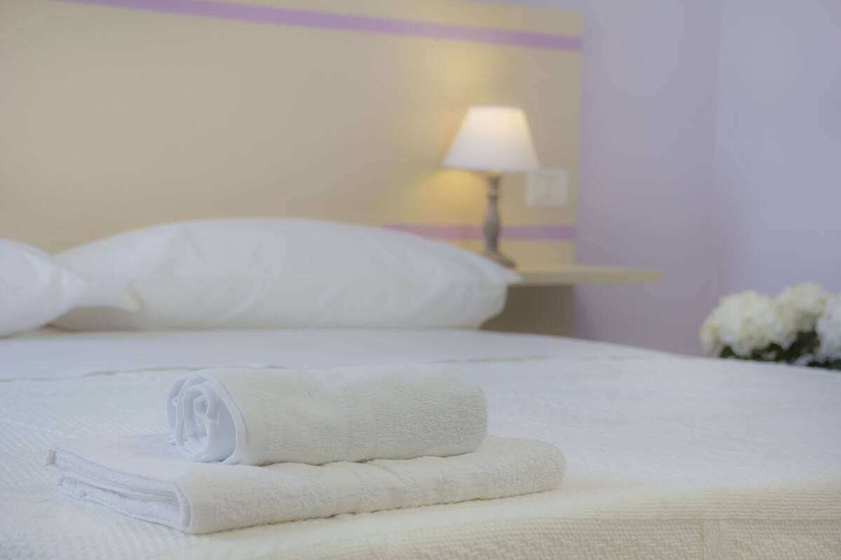 A neatly made bed with white linens, a lamp on a bedside table, and a vase with flowers.