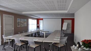 A conference room with a long table, chairs, a whiteboard, and a projector screen.