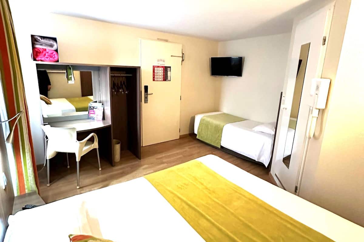 Una habitación de hotel con cama, escritorio, silla, televisor y armario.