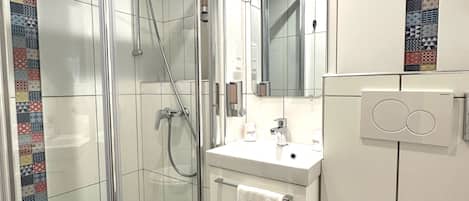 Un baño moderno con ducha de vidrio, lavamanos blanco y retrete.