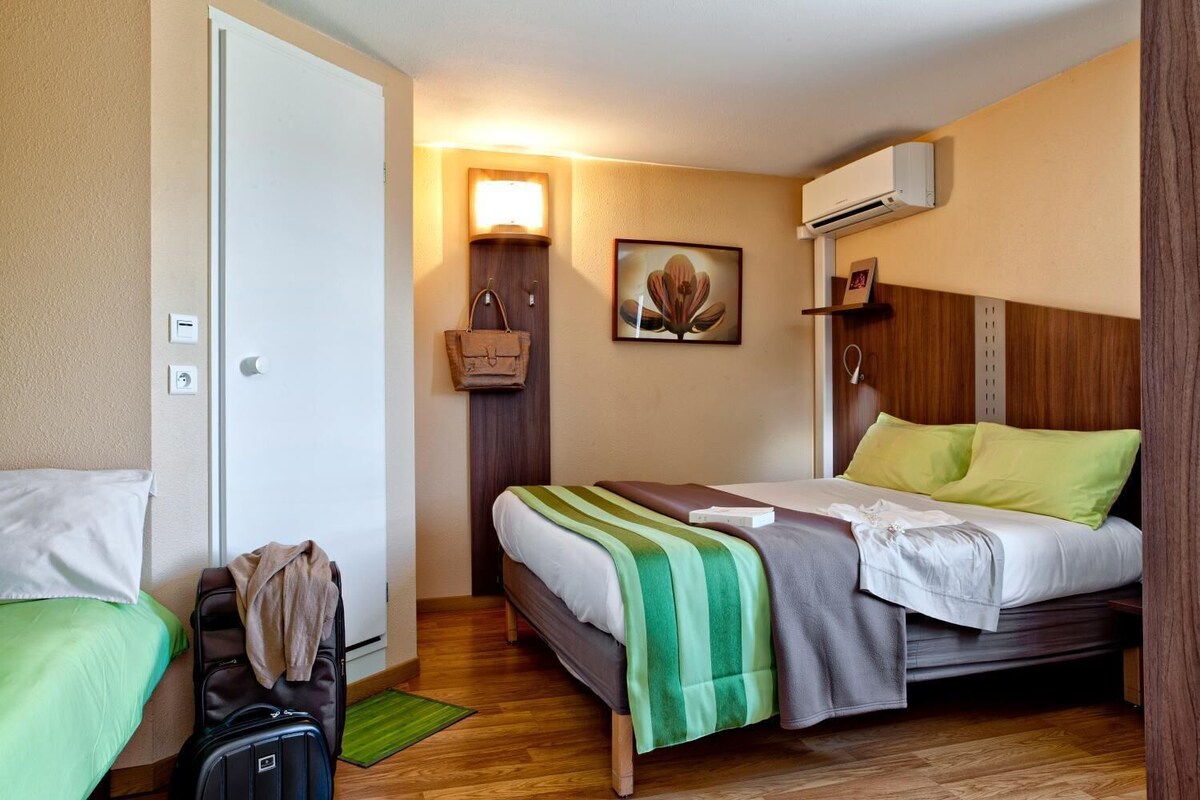 A hotel room with two beds, a suitcase, a wall-mounted air conditioner, and a framed artwork.