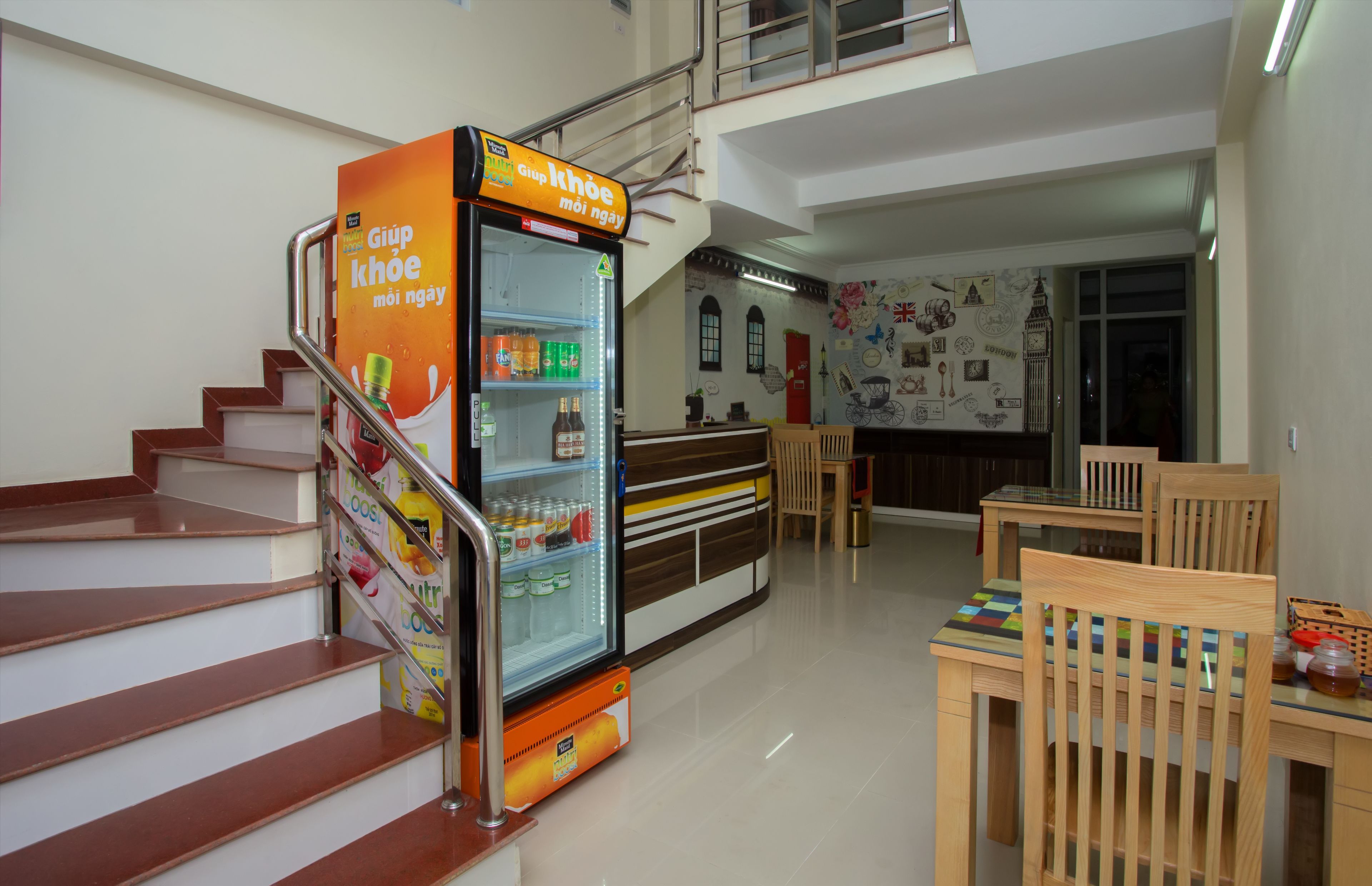 A staircase leading to a second floor, a vending machine with beverages, and a dining area with wooden chairs and tables.