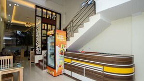 Un hall d’hôtel moderne avec un escalier, un comptoir d’accueil et une vitrine réfrigérée.