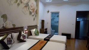 Une chambre d’hôtel avec deux lits, une décoration murale florale, une petite table et une salle de bain visible à travers une porte ouverte.