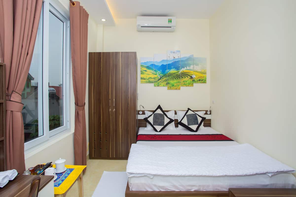 Habitación de hotel con cama, armario, ventana con cortinas, un cuadro en la pared y aire acondicionado.