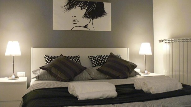 A neatly made bed with striped bedding and two pillows, flanked by bedside lamps on white nightstands. - Ager Vaticanus (Rome)