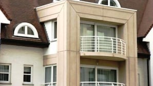 A multi-story building with a beige facade, multiple windows, and a balcony with a white railing. - Knokke-Zoute - Exclusive Sun and Sea Village Near Bruges (Knokke-Heist)