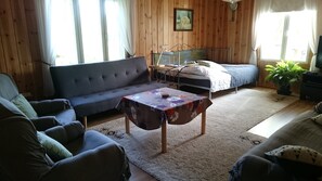 Relax in this inviting room with a comfortable sofa, a small table, and a bed, surrounded by natural light and a touch of greenery.