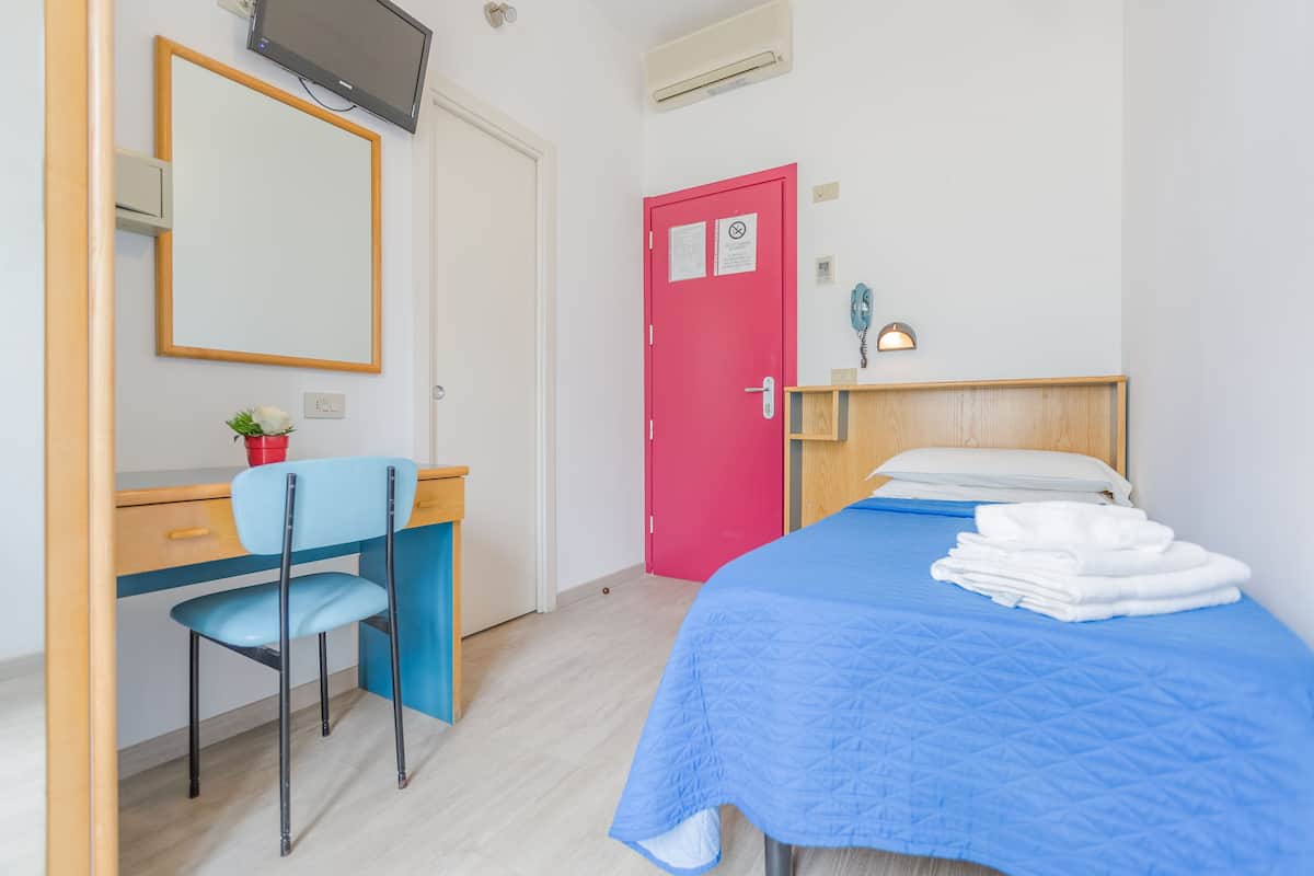 A bedroom with a bed, a desk with a chair, a television, and a red door.