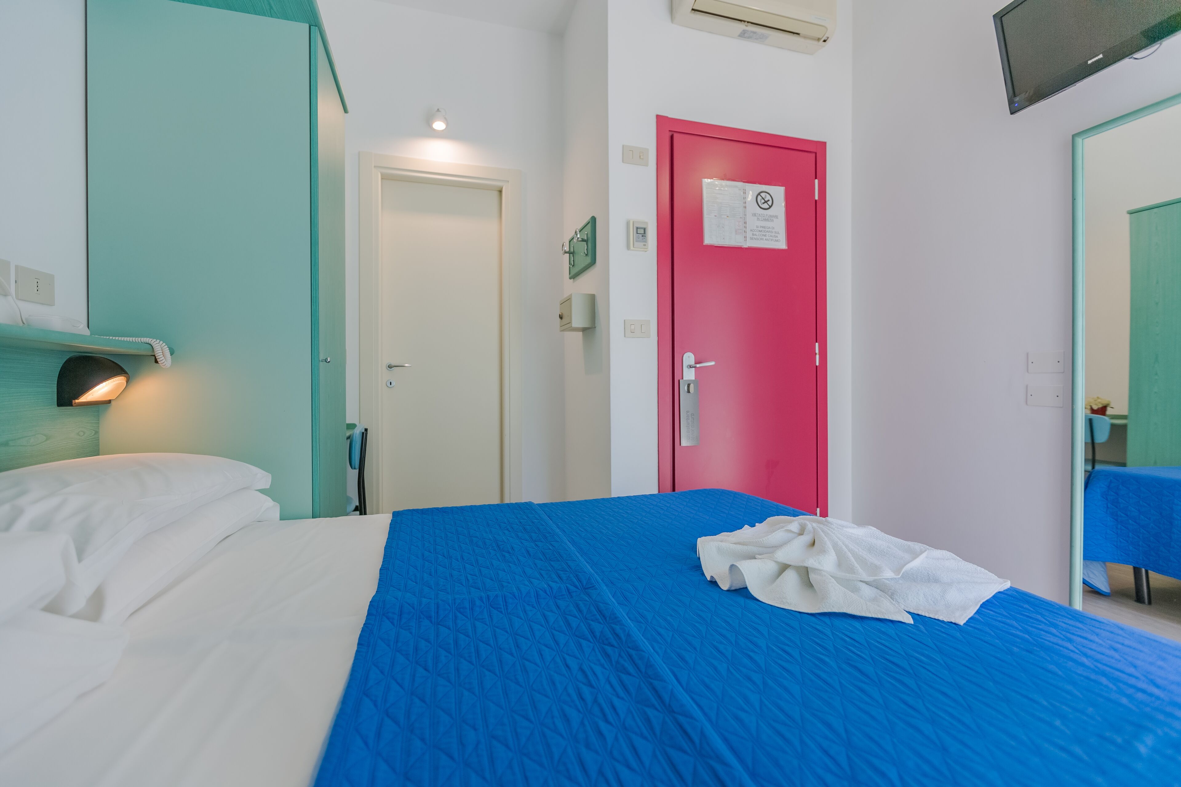Et hotelværelse med seng, rød dør, fjernsyn og badeværelse med spejl.