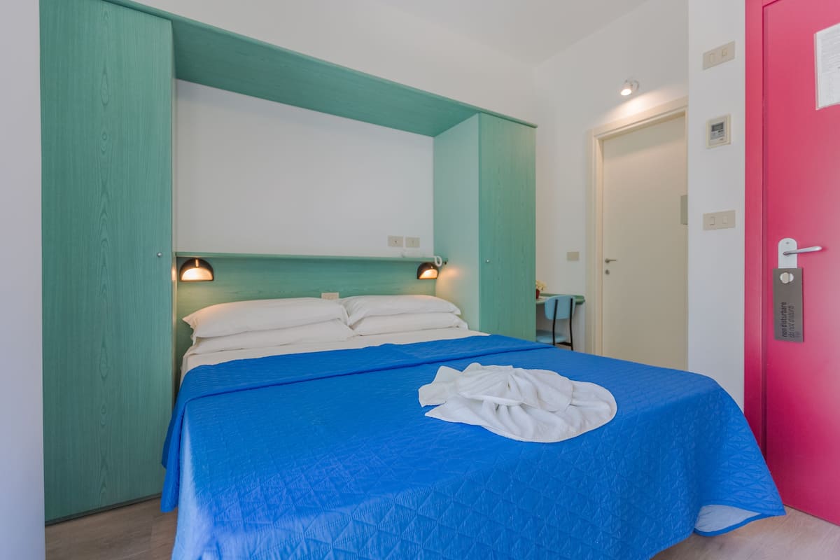A room with a bed, a blue bedspread, and a white towel on the bed.
