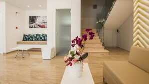 Un intérieur moderne avec un escalier, un canapé, un vase blanc rempli de fleurs et un tableau encadré accroché au mur.