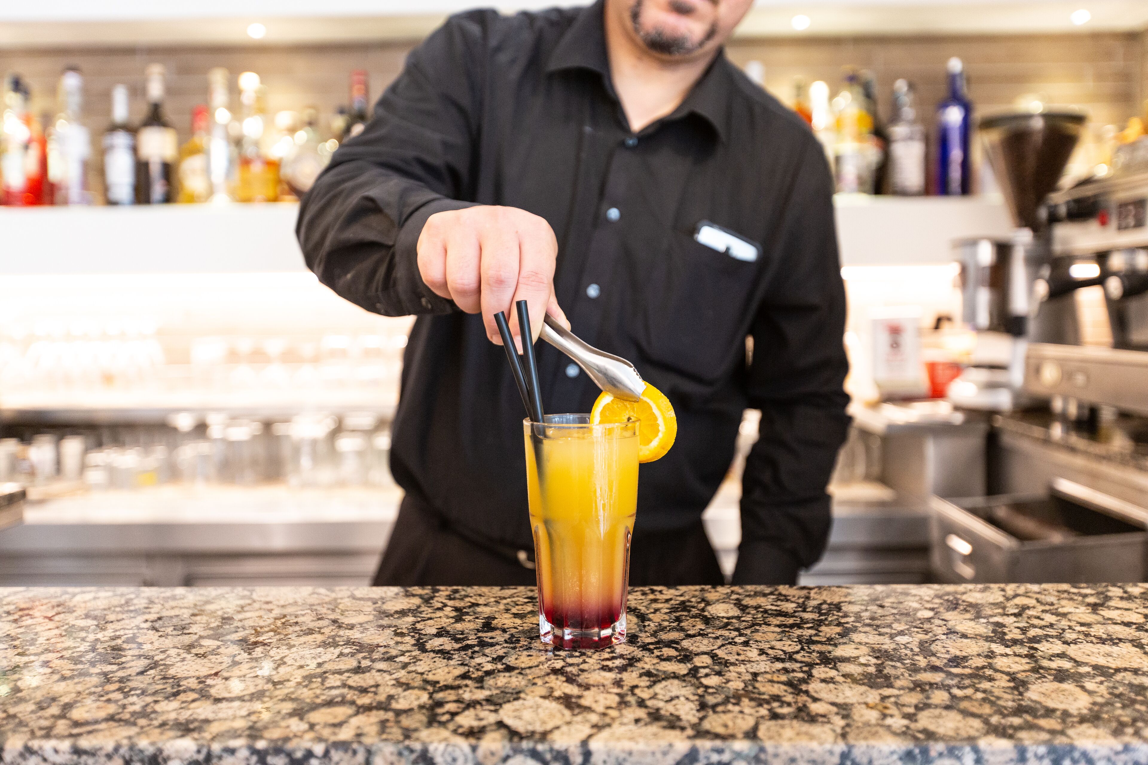 Ein Barkeeper bereitet ein Getränk mit einer Limettenscheibe und einem Strohhalm zu.