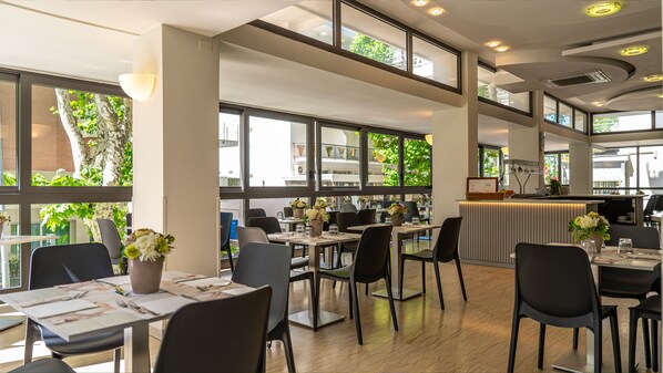 Ein modernes Restaurant mit hohen Decken, großen Fenstern und einem klaren, übersichtlichen Design.