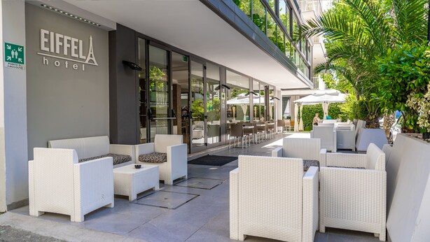 Un espace extérieur aménagé avec des meubles en osier, une entrée en verre donnant sur l’hôtel et une vue sur la rue.