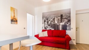 Un salon moderne avec un canapé rouge, une table blanche et une fresque représentant un paysage urbain sur le mur.