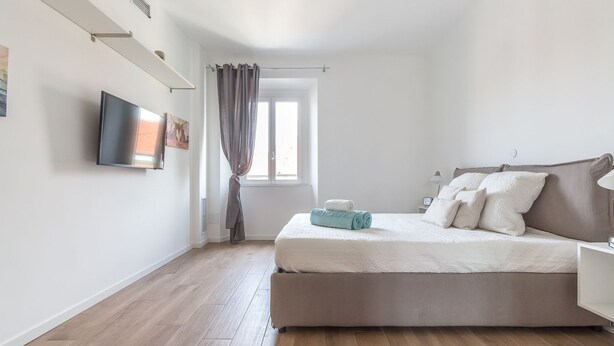 Une chambre à coucher avec un lit, une télévision, une fenêtre avec des rideaux et un plancher en bois.