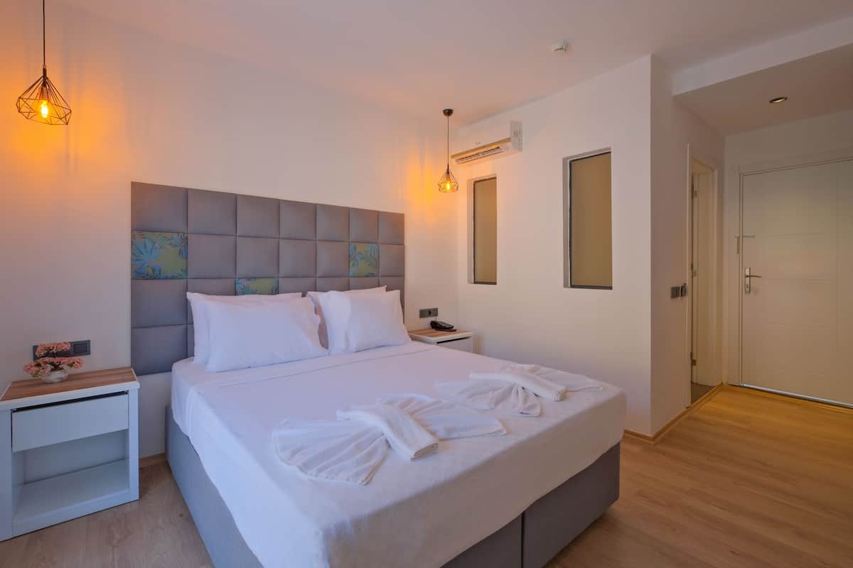 A modern hotel room with a large bed, bedside tables, a headboard with artwork, and a wardrobe.
