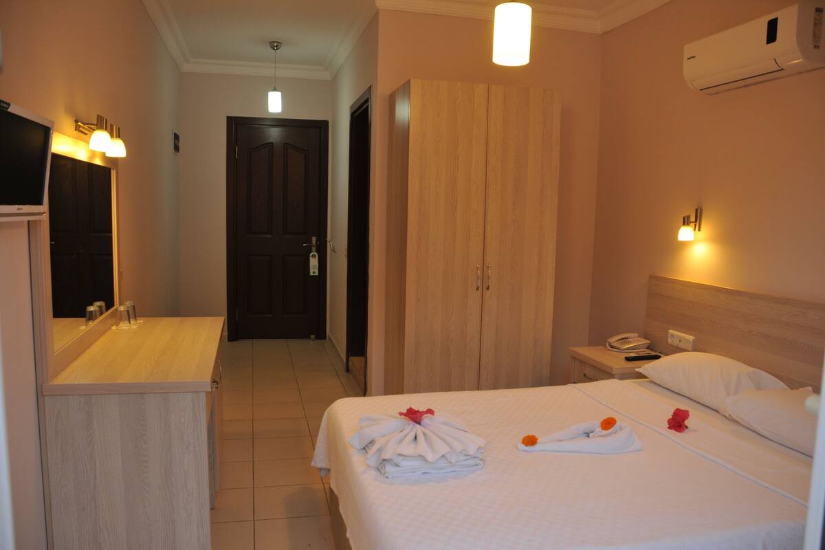 A hotel room with a bed, a wardrobe, a bedside table with a phone, and a mirror.