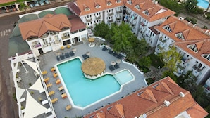An aerial view of a hotel with a central swimming pool, multiple balconies, and outdoor seating areas.