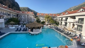 A hotel pool area with a central water feature, lounge chairs, and a thatched structure.
