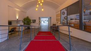 A hotel lobby with a red carpeted staircase, a reception desk, and a large window with a view of the outside.