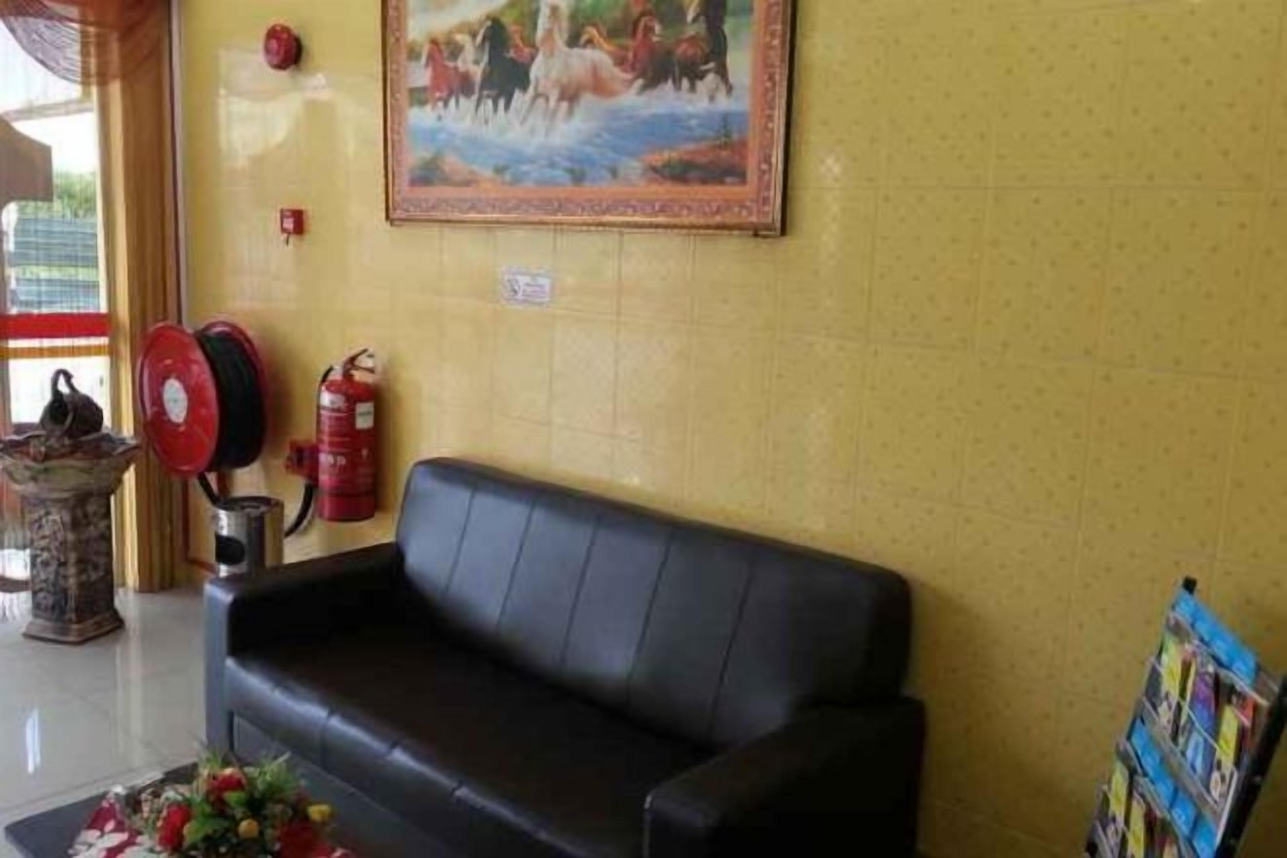 A lobby with a black leather sofa, a fire extinguisher, a fire hose reel, and a painting on the wall.