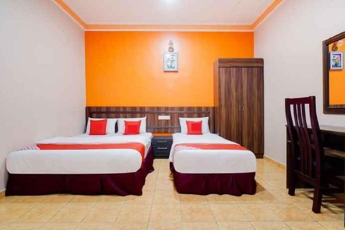 A hotel room with two beds, a wooden wardrobe, a desk, and a chair.