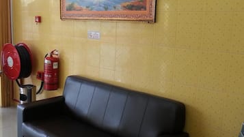 A black leather sofa against a yellow wall with a painting of horses, a fire extinguisher, and a fire alarm.