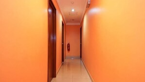 Un couloir avec des portes de part et d’autre, un extincteur accroché au mur et un sol carrelé.