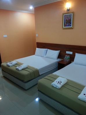 A hotel room with two beds, each with a pillow and a towel. There is a nightstand with a lamp and a small table with bottles. - Bercam Times Inn Hotel (Ipoh)