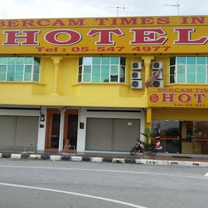 Un bâtiment jaune avec une enseigne indiquant « Bercam Times In Hotel » et un numéro de téléphone.